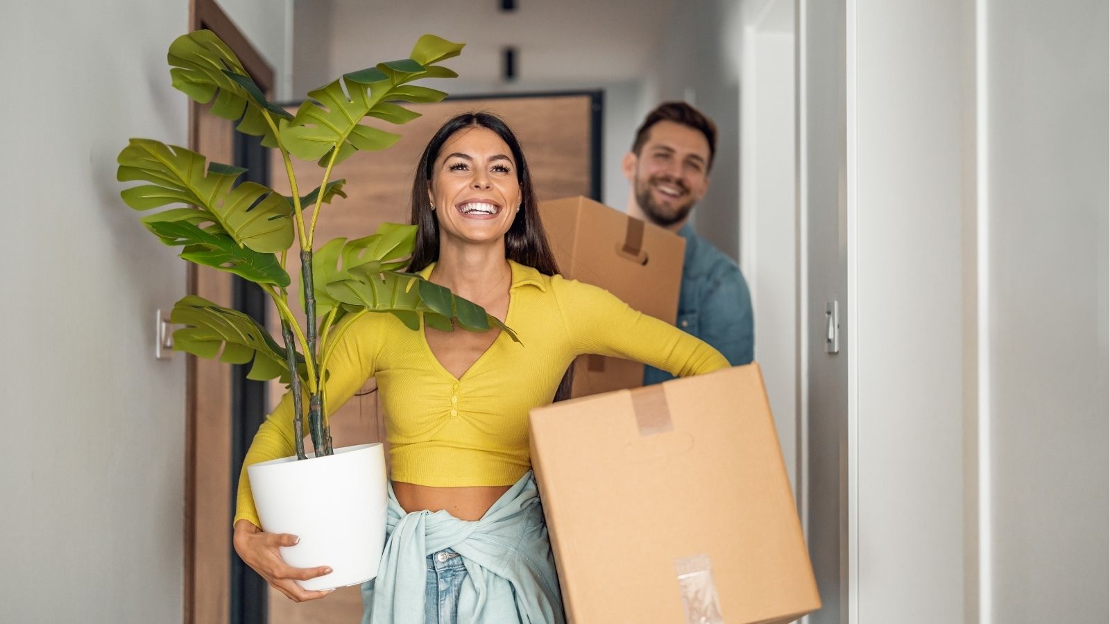 happy couple carrying moving boxes and a plant