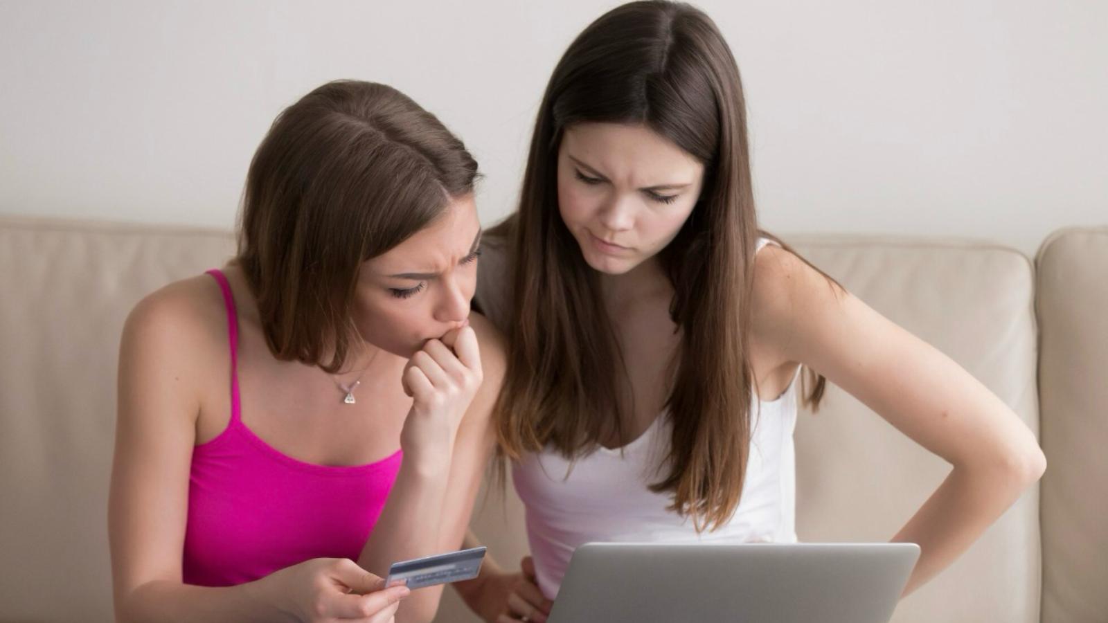 Two teenage girls trying to figure out how tomake online payment while holding a credit card