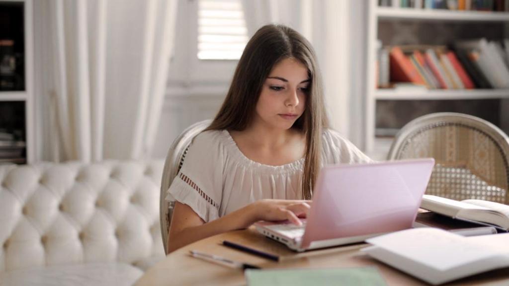 Teenage girl seriously studying with her laptop and books