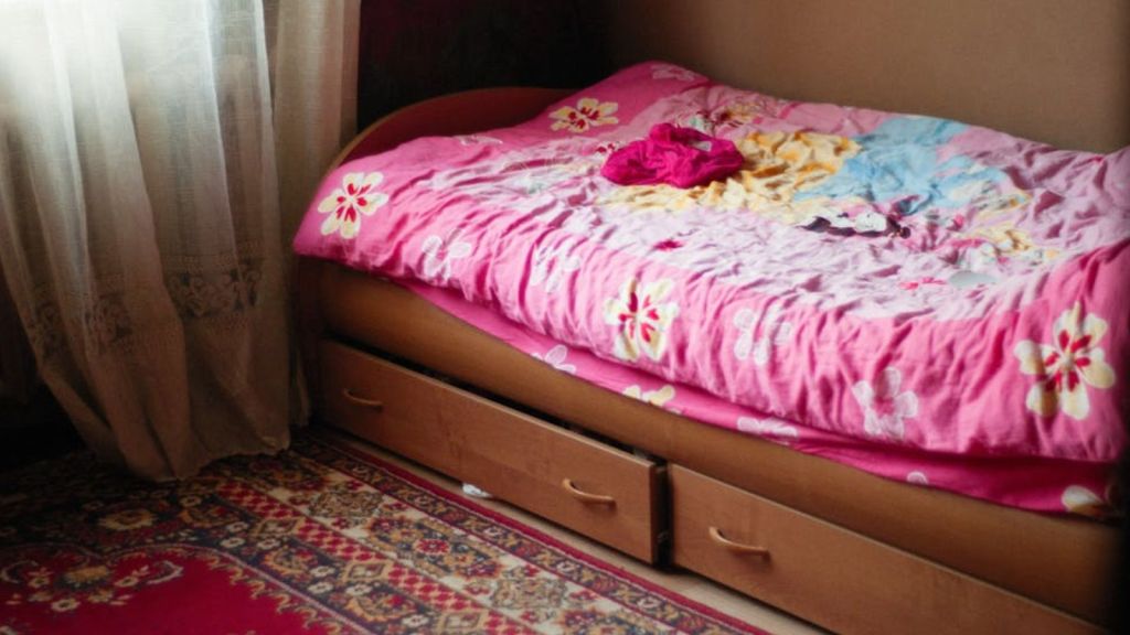 A pink mattress on top of a wooden bed frame with drawers