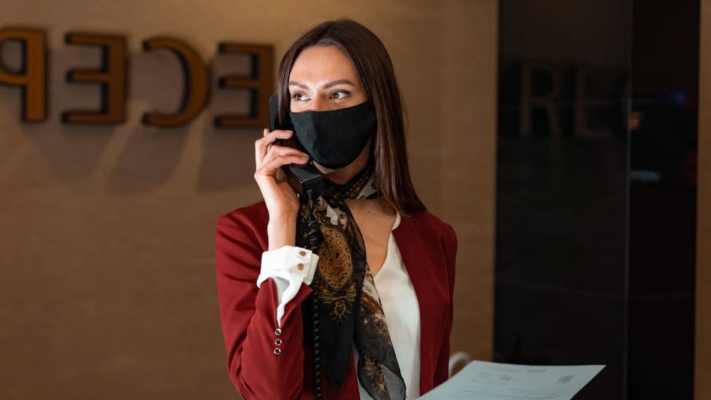 Hotel front desk employee with facemask talking on the phone