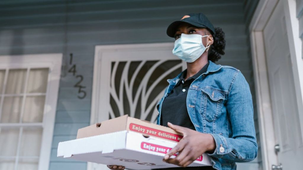 Female food delivery driver holdng two boxes of pizza in front of a door