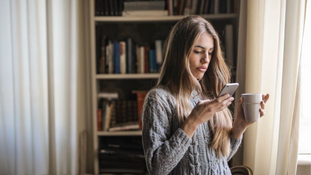 Woman looking at her phone while holding a mug