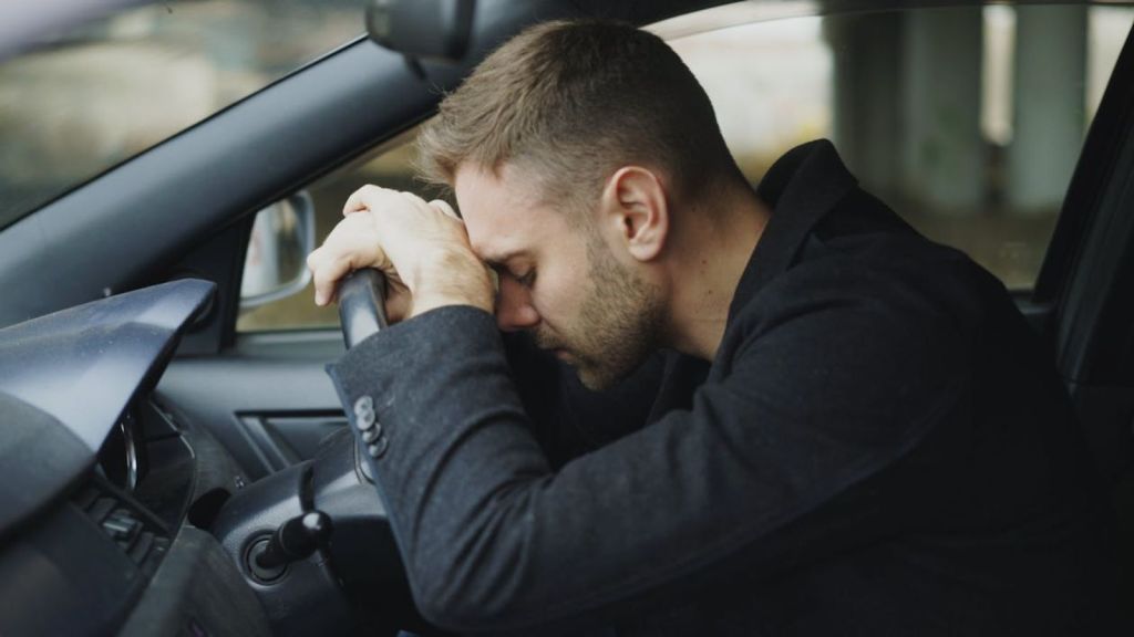 Tired man waiting in the car with his head on the steering wheel