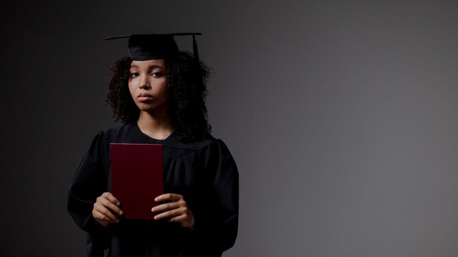 Sad teenage girl in graduation gown holding her diploma