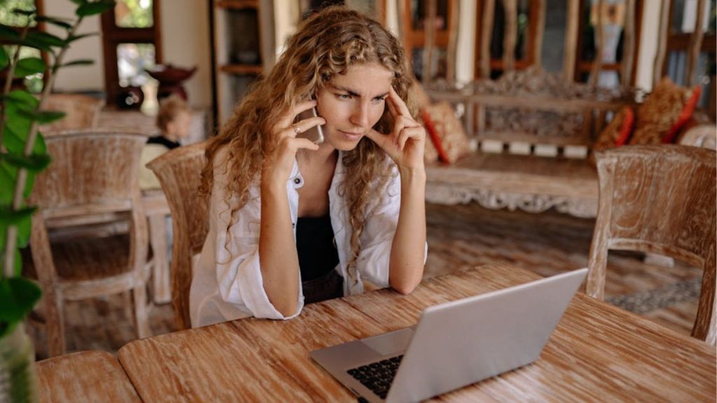 Woman looking at her laptop while talking to someone on her phone