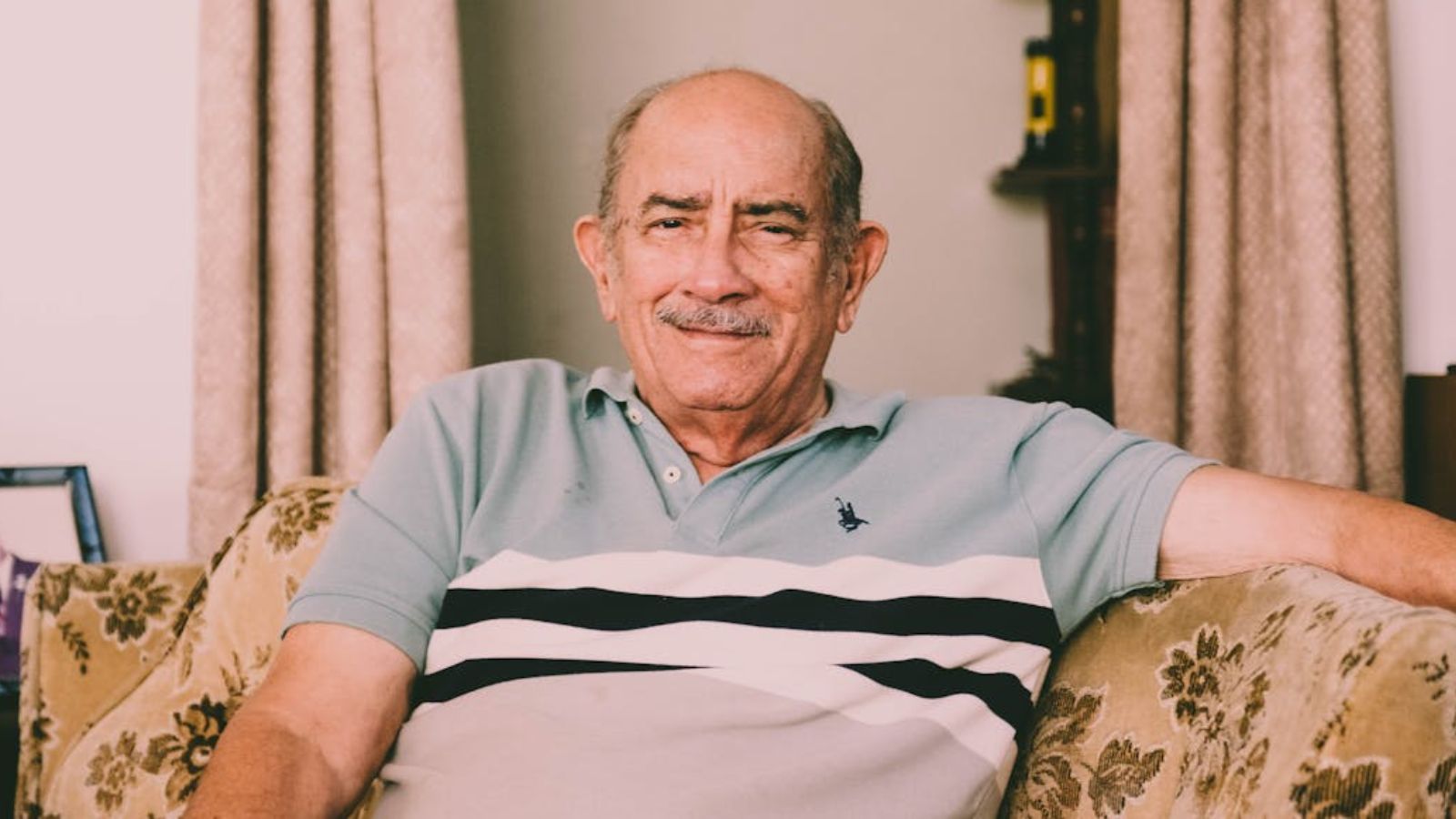 A cheerful elderly man enjoys a relaxed moment on a sofa in a warmly decorated living room