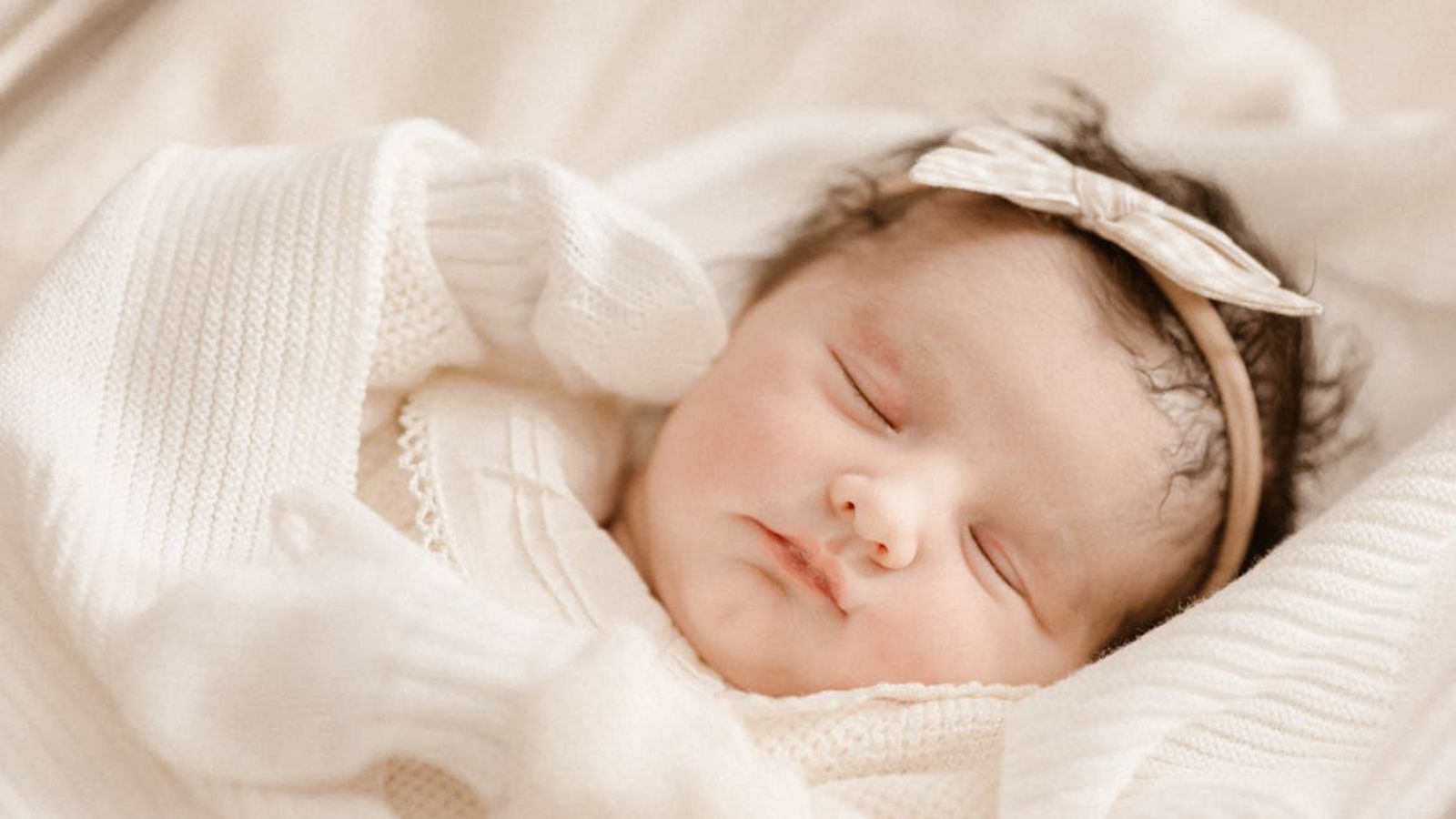 Newborn baby girl wearing a dress and head bow sleeping