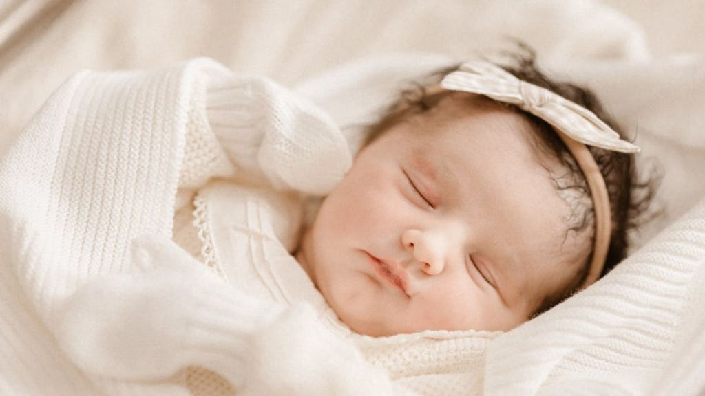 Newborn baby girl wearing a dress and head bow sleeping