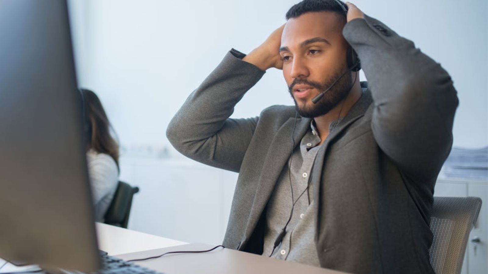 Call support employee looking at his computer with his hands on the back of his head