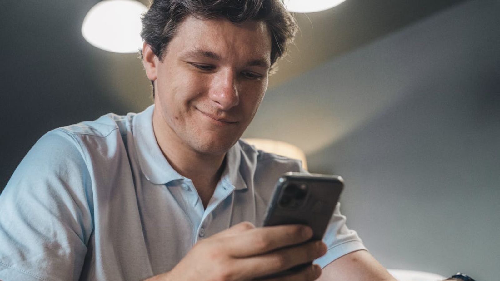 The Loudspeaker War: Why a Polite Restaurant Request Exploded Into a Hilarious Battle of Petty Auditory Retaliation Man in a blue polo shirt smiling while using a smartphone