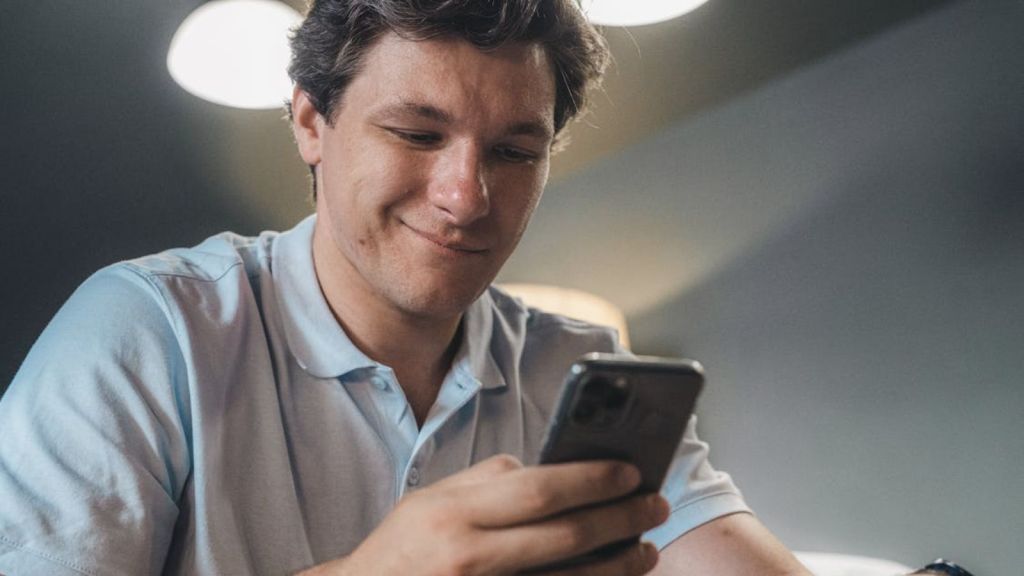 Man in a blue polo shirt smiling while using a smartphone