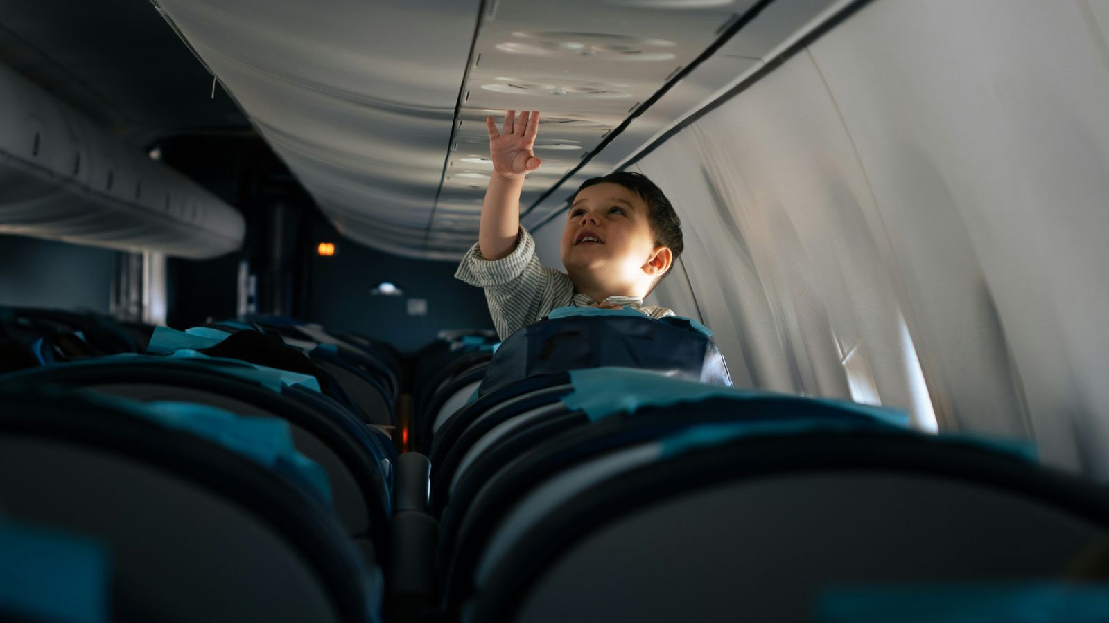 Woman Asks Parent to Quiet Loud Child on Red Eye Flight, but the Request Is Ignored Curious child reaching up to the overhead panel inside an airplane cabin