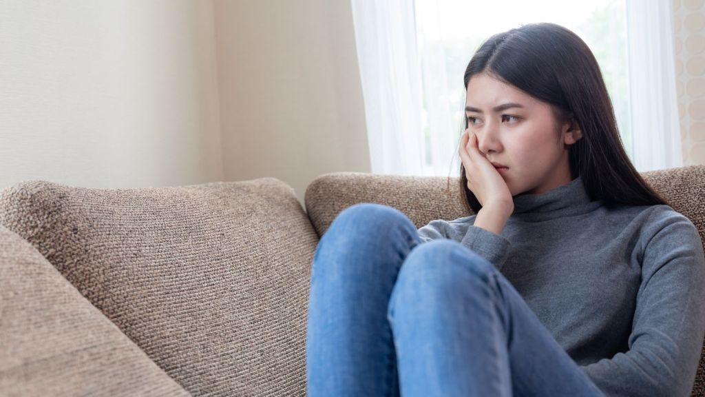 Young Asian woman feeling sad while sitting on a couch