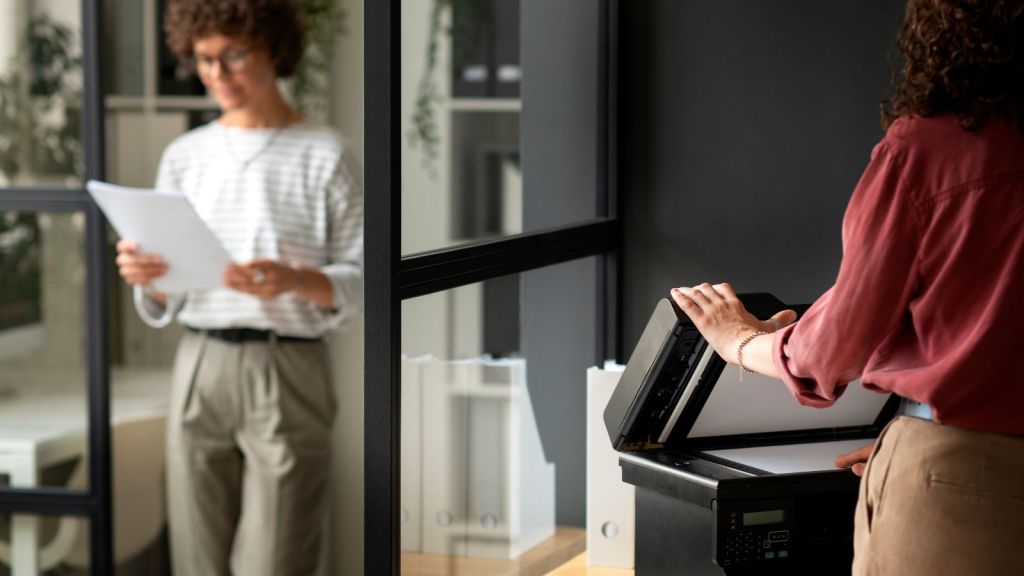 One employee holding documents and another one printing on a printer