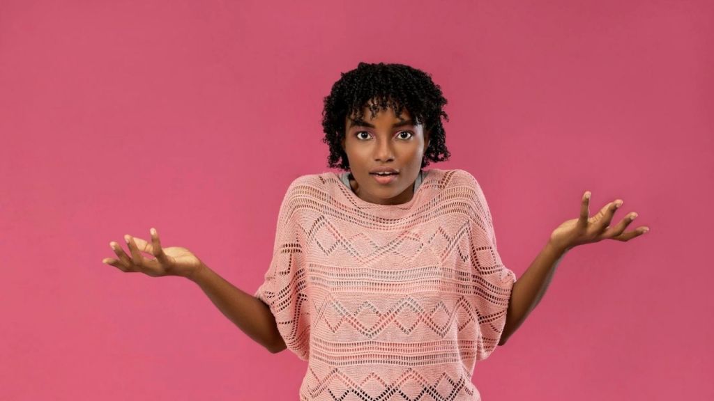 woman shrugging against a pink background