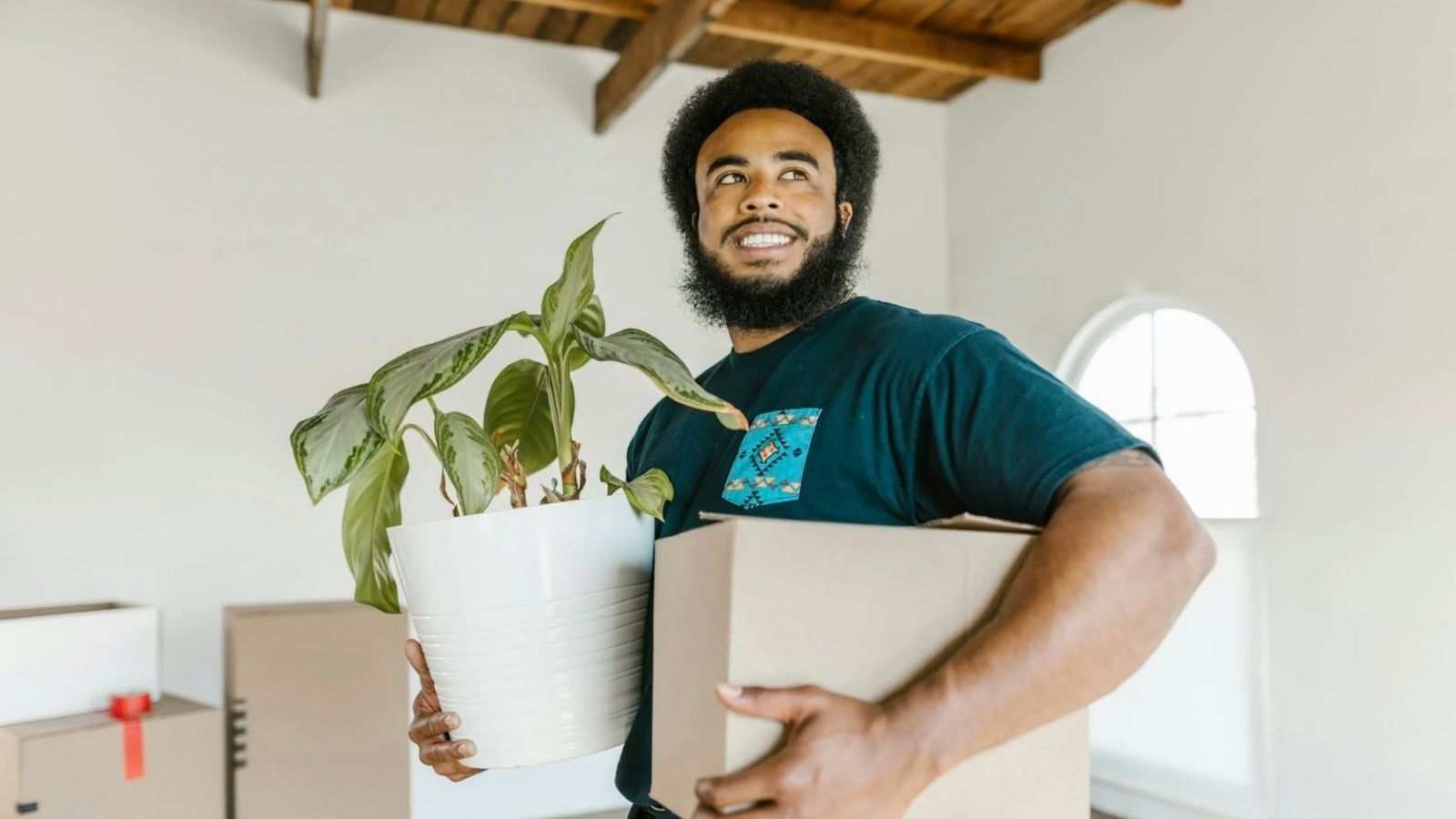 He Finally Left His Slumlord’s House. Then Came the Fake Damage Claim smiling man holding a moving box and a plant
