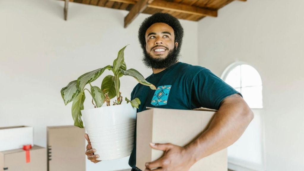 smiling man holding a moving box and a plant