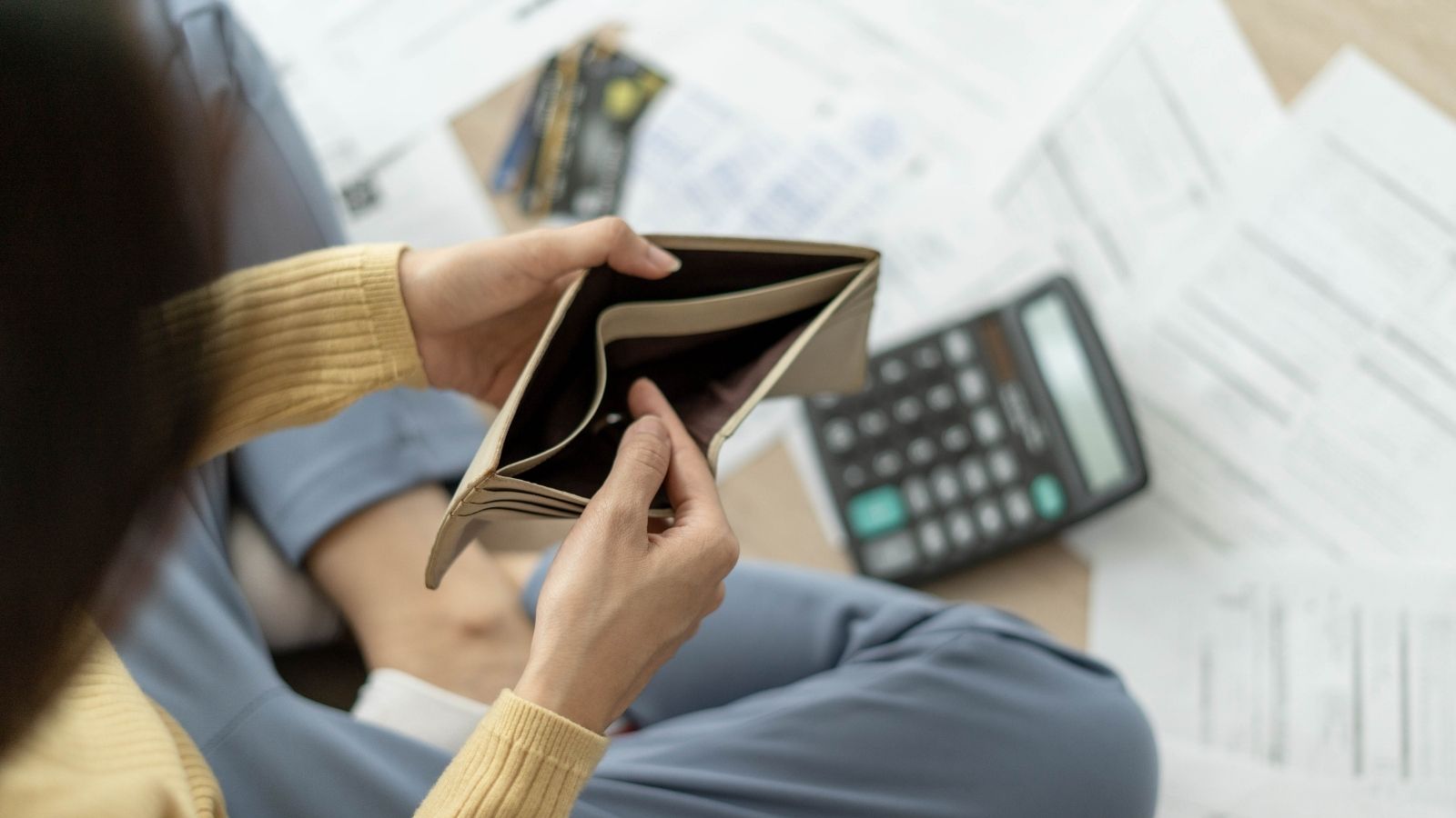 woman with an empty wallet surrounded by bills that need to be paid