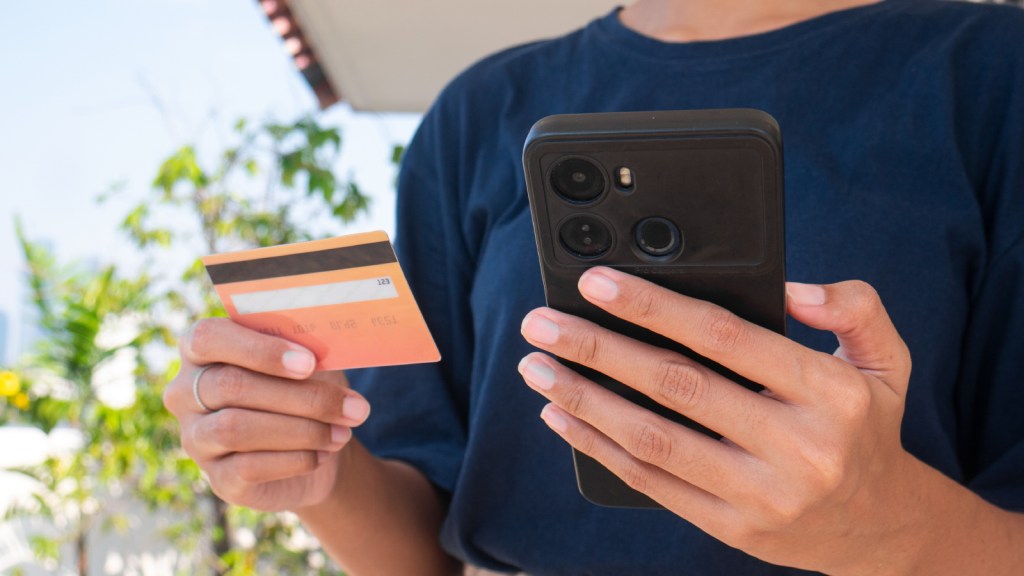 A woman holds a smart phone in one hand and a credit card in the other