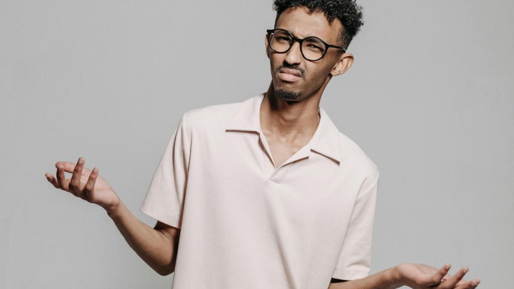 confused man in beige polo and glasses shrugging