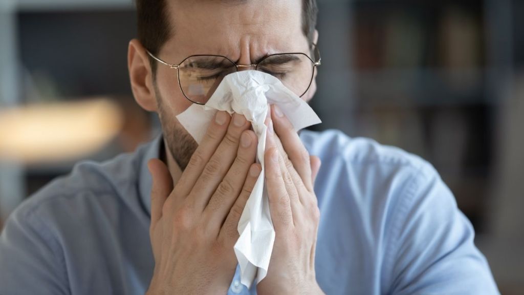 man sneezing into a kleenex