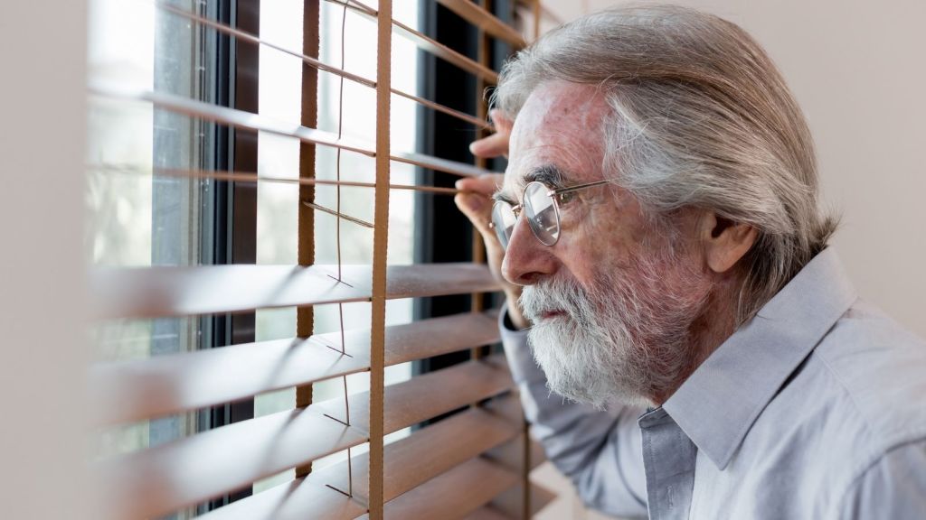 older man looking out mini blinds