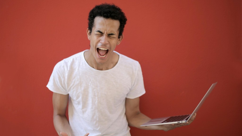 A man holding a laptop and shouting.