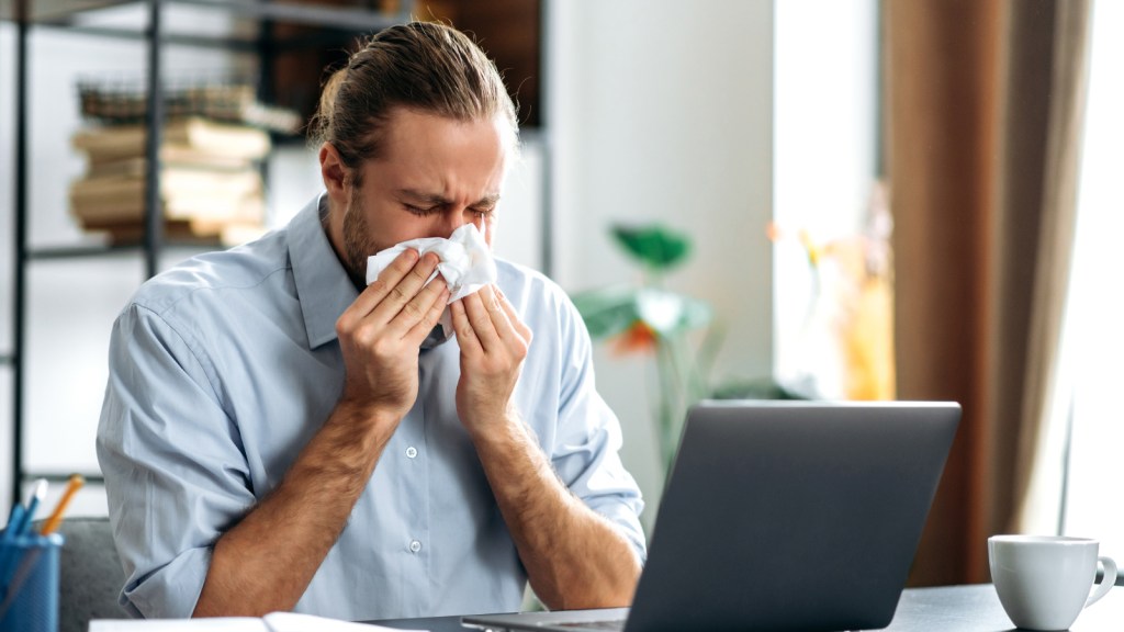 A man blowing his nose at his desk