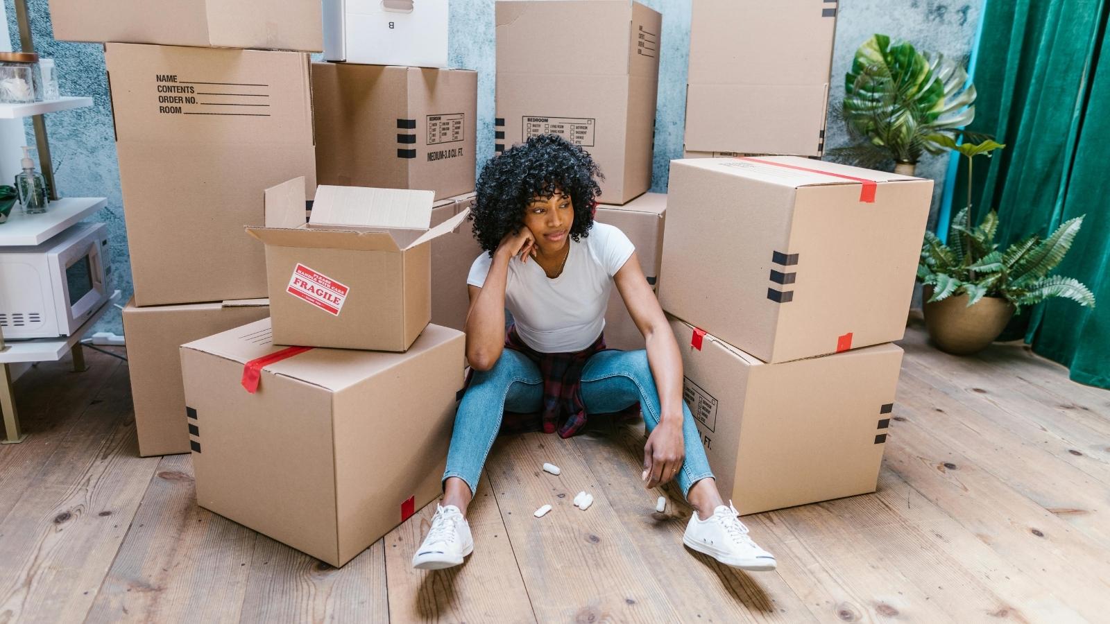 She Thought Moving in With Her Sister Would Save Her Money. Instead, It Triggered a Crucial Fight for Independence woman sitting in front of a pile of moving boxes