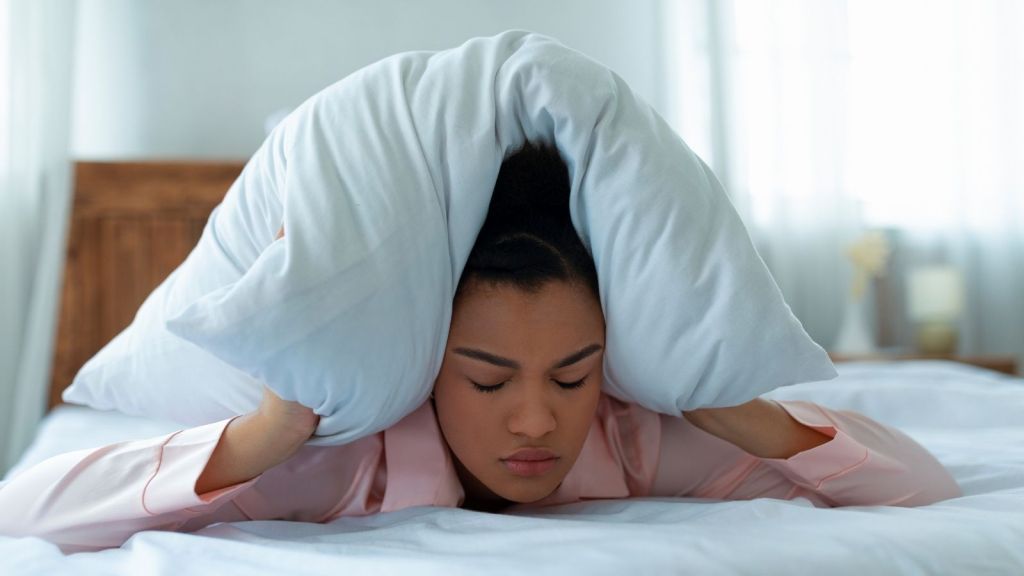 annoyed woman covering her head with a pillow