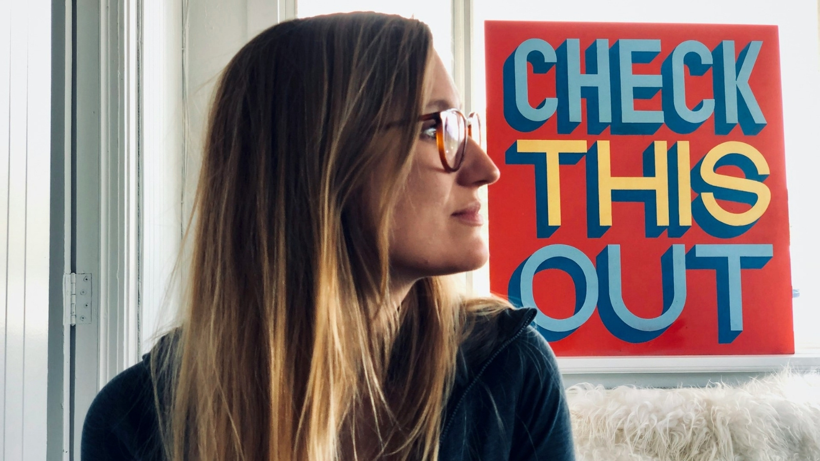 Woman wearing glasses beside a sign