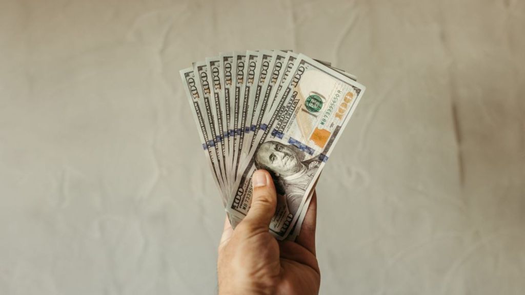 A person's hand holding several 100-dollar bills