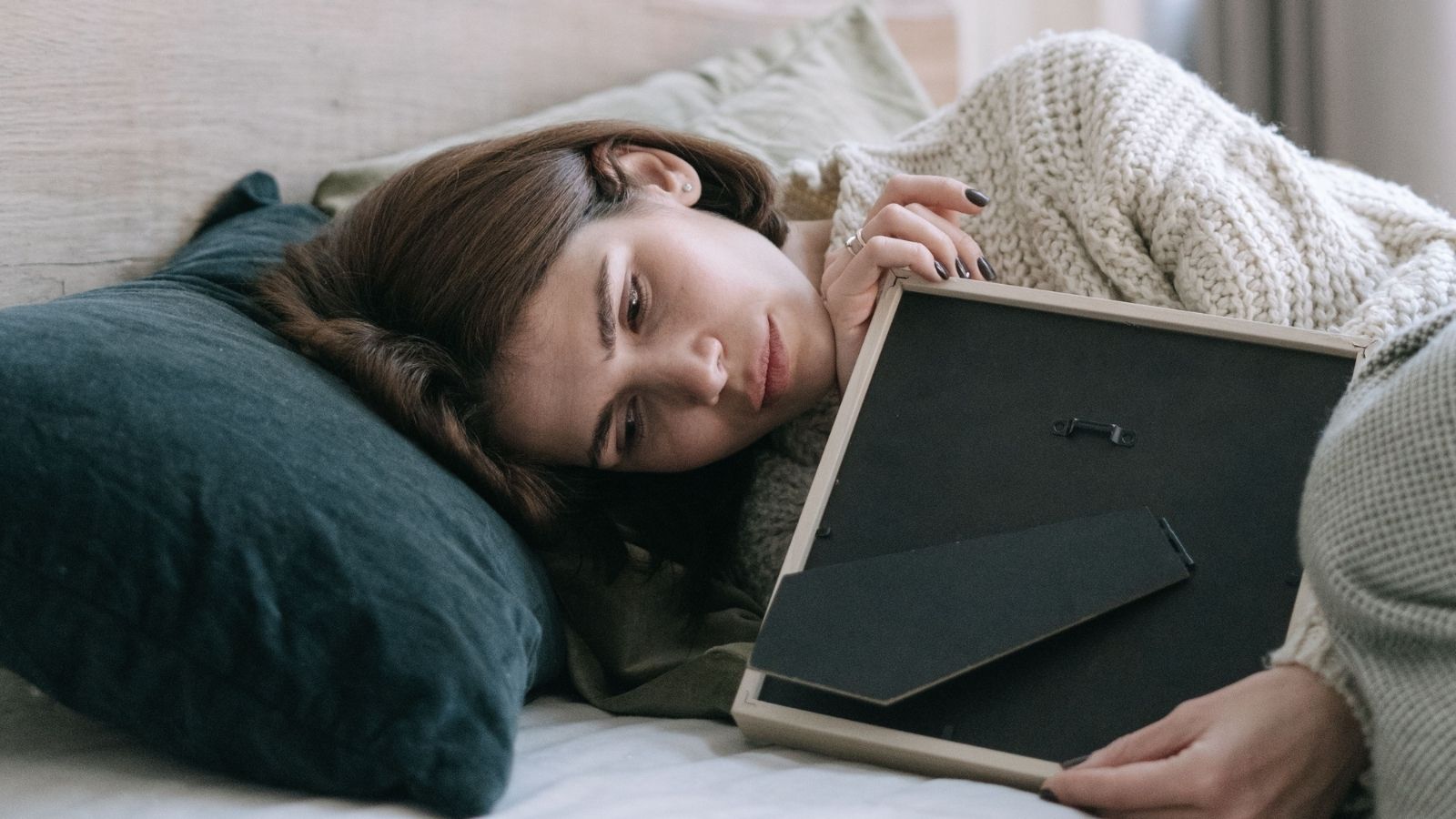 A Woman Is Grieving Her Grandmother’s Sudden Passing, But Her Husband Is More Concerned About Watching Hockey With His Brother A sad woman clutching a photo frame