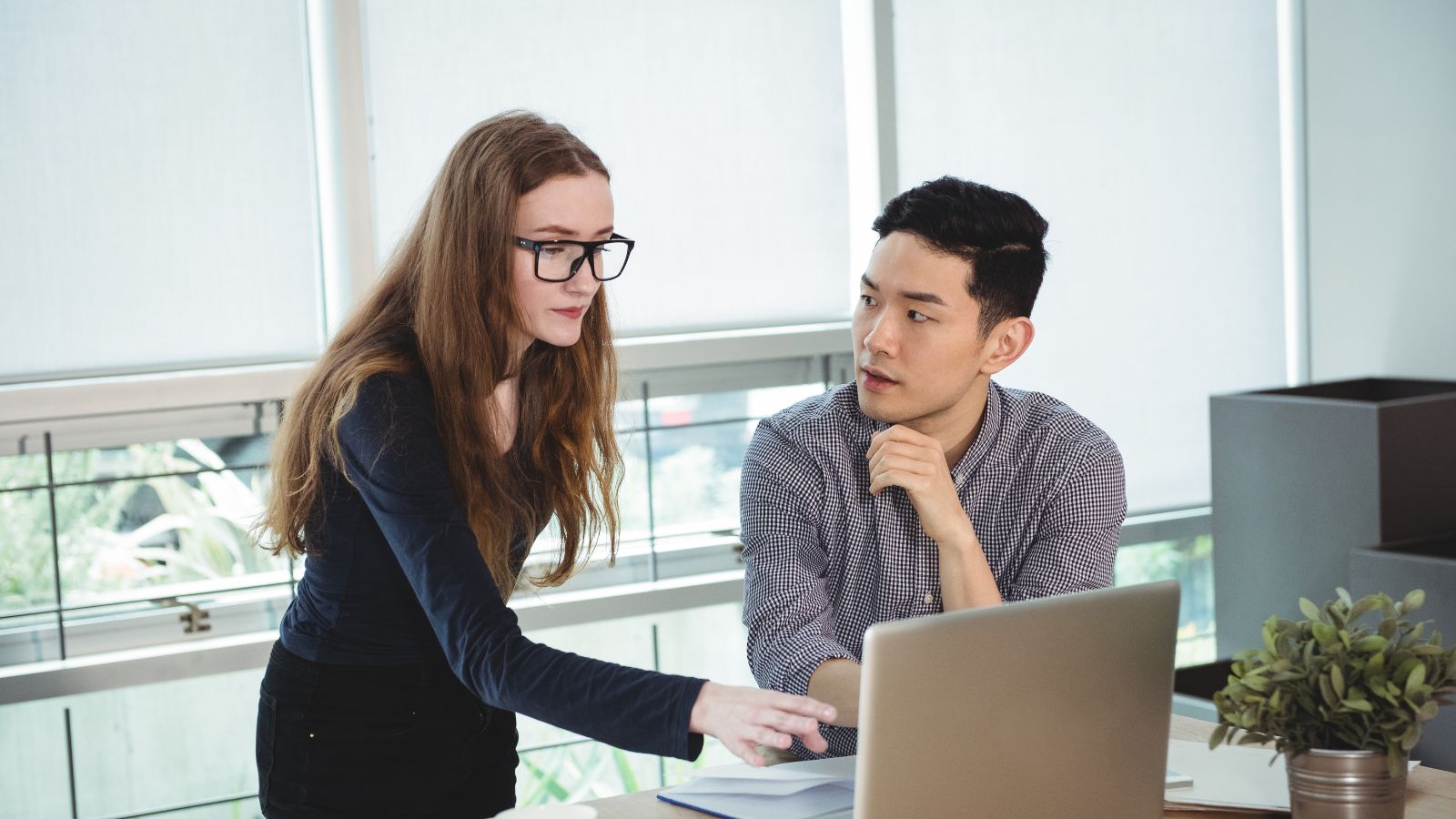 Female employee giving instructions to her colleague in front of a computer