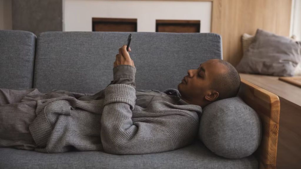 Man lying on the couch while using his phone
