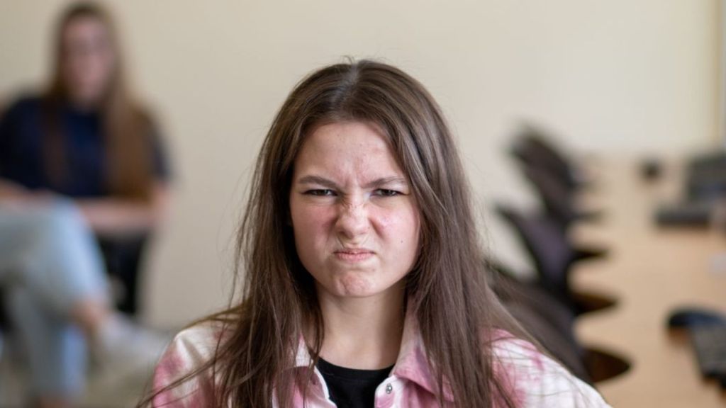Teenager frowning while a person is in the background