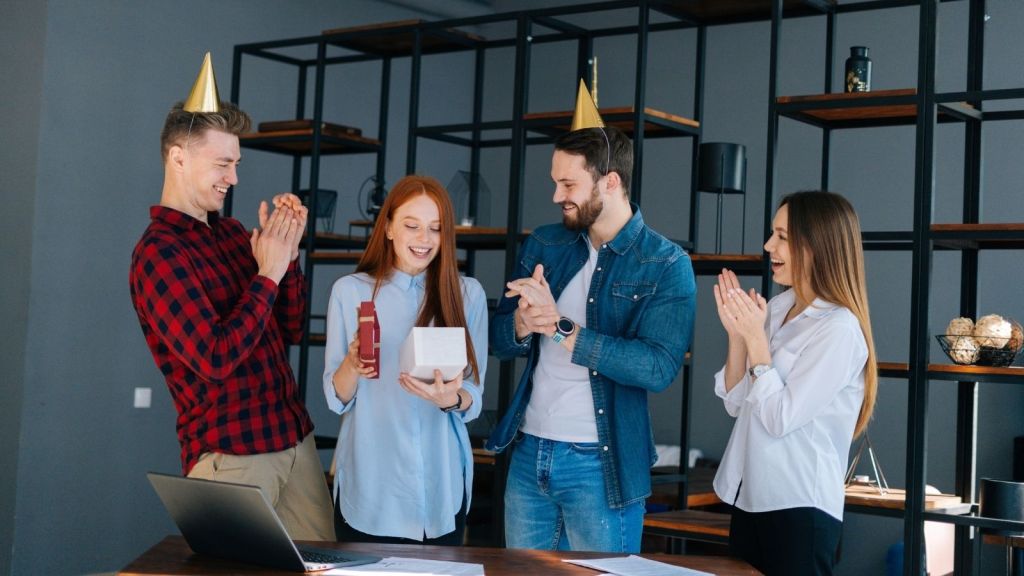 woman opening birthday present at work with coworkers