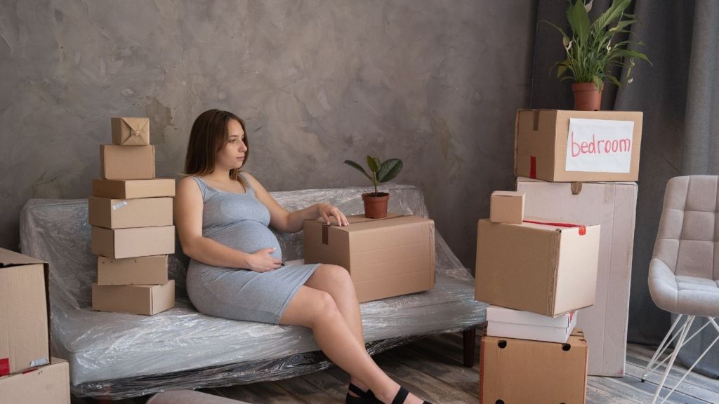 pregnant woman sitting on couch surrounded by moving boxes