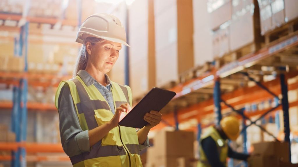 woman in a hardhat looking at a tablet in a distribution center