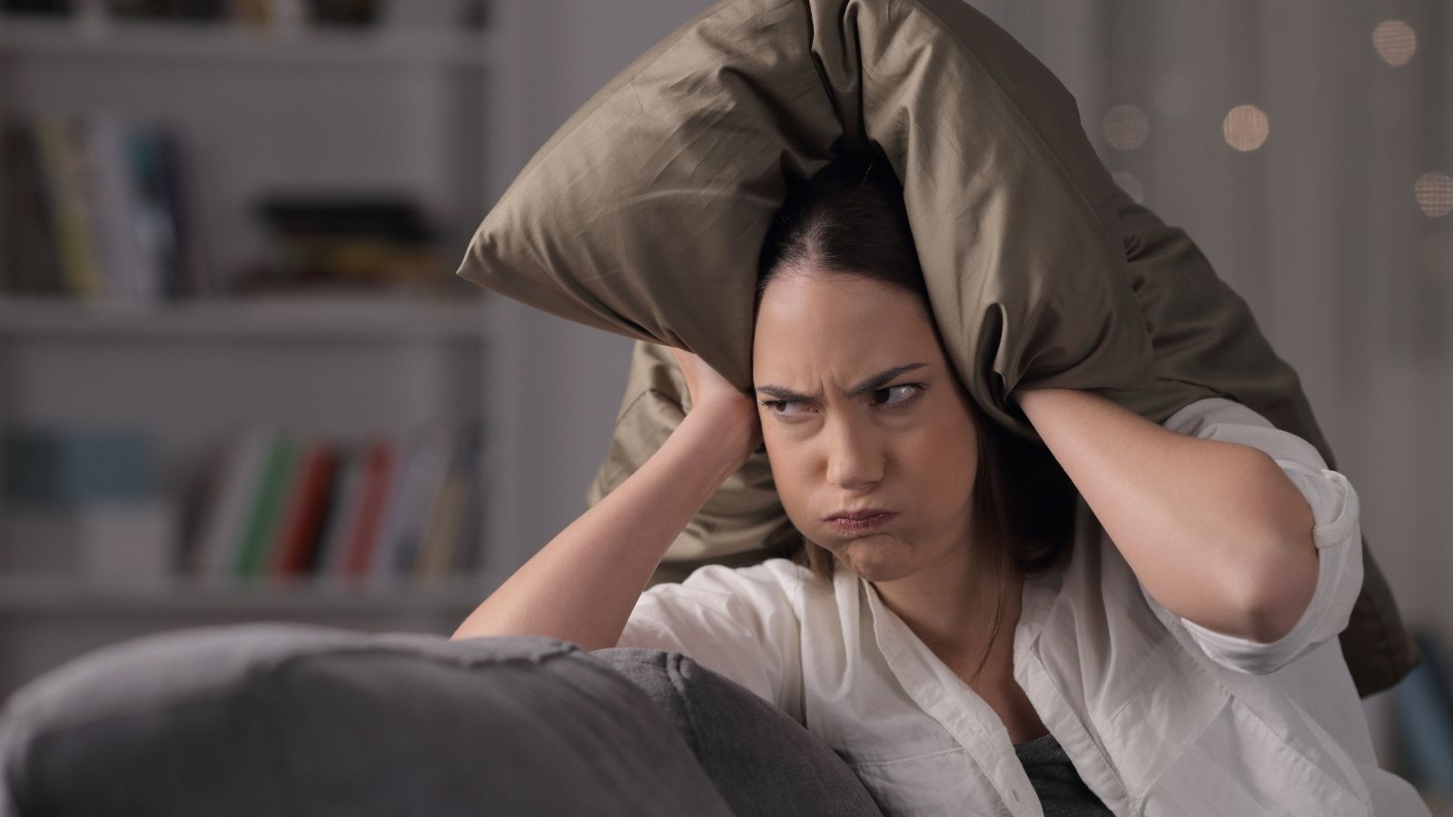 Exhausted Townhome Owner Says Nothing Works to Stop the Constant Noise From Next Door upset woman with a pillow on her head to block out noise