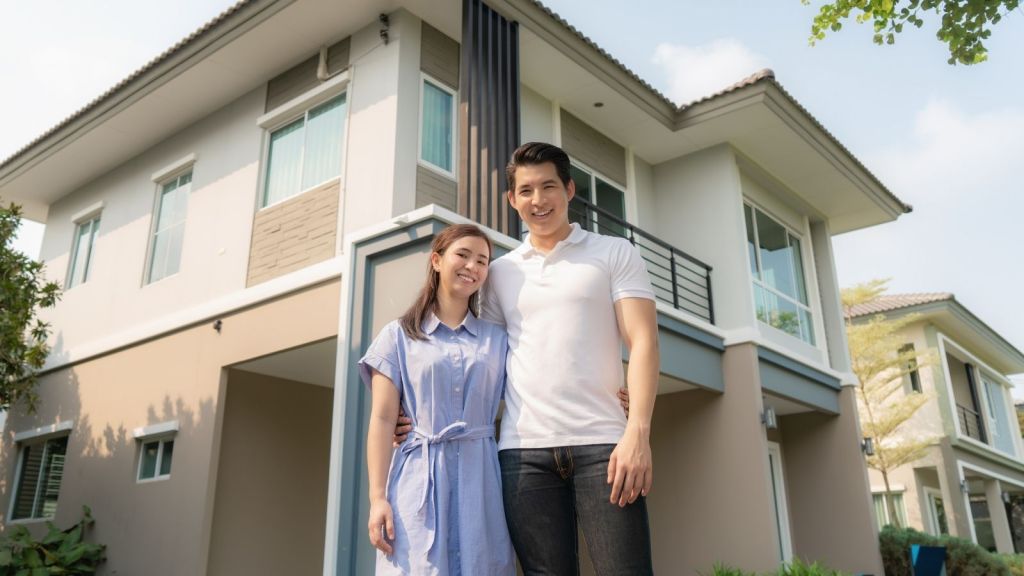 happy young couple standing in front of their house