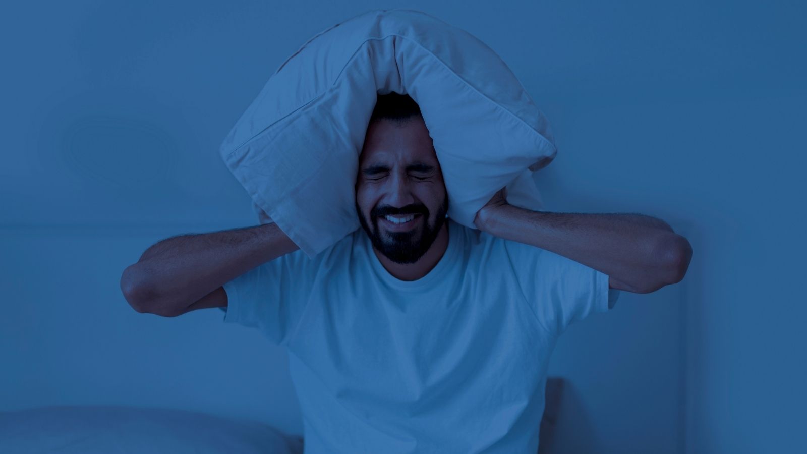 man trying to block out noise with a pillow