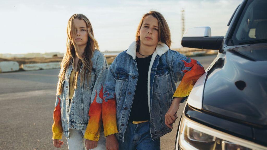 two teenagers standing next to a car in a parking lot