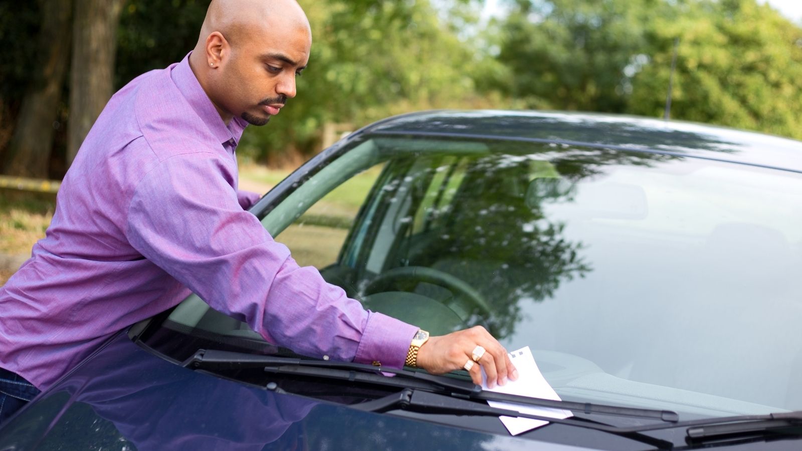 man picking up a note someone left on the windshield of his car