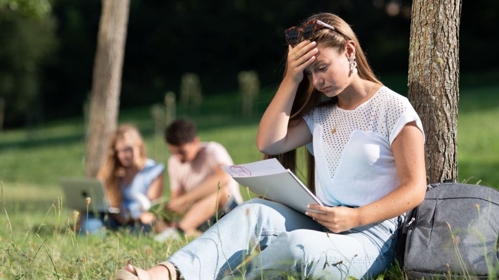 frustrated young woman sitting on the grass looking at a bad grade