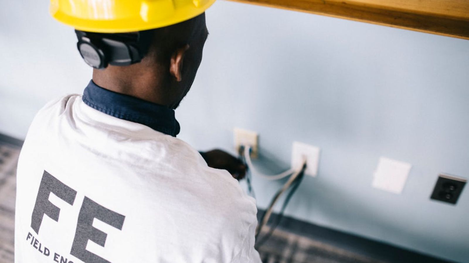A field engineer in a hard hat working on electrical installation indoors