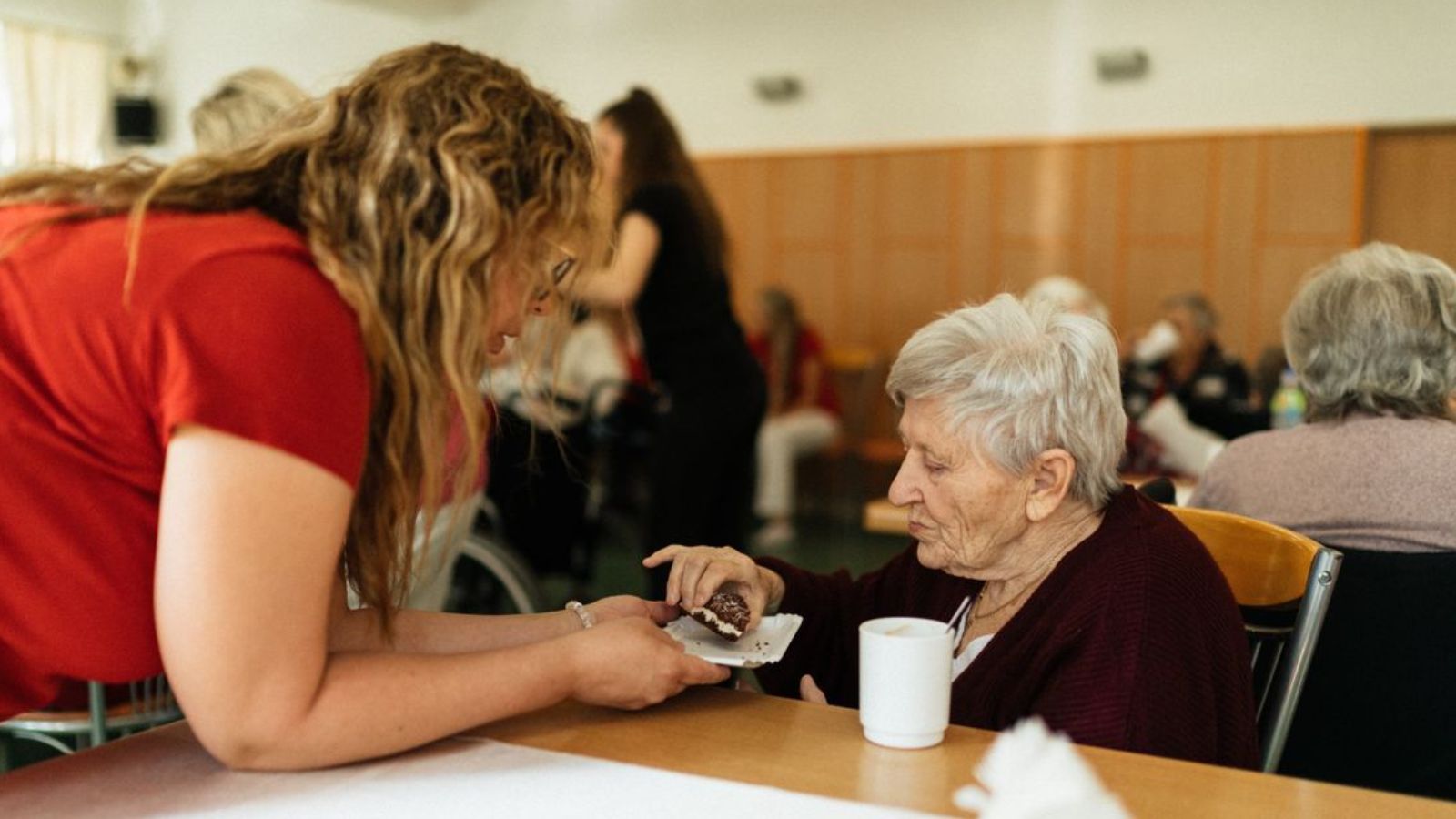 Man Refused to Take His Mother Out of Memory Care to Fund His In Laws’ Housing, so He Was Accused of Being Unfair and Inconsiderate An elderly woman being assisted by a caregiver in a nursing home setting