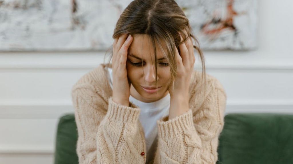 Woman sitting on a sofa holding her head, expressing stress and frustration