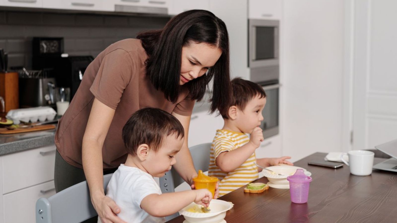 Stay at Home Mom Wants a Day to Herself for Her Birthday, but Her Husband Thinks She’s Being Unreasonable Mother helping her toddlers enjoy breakfast in a modern kitchen setting